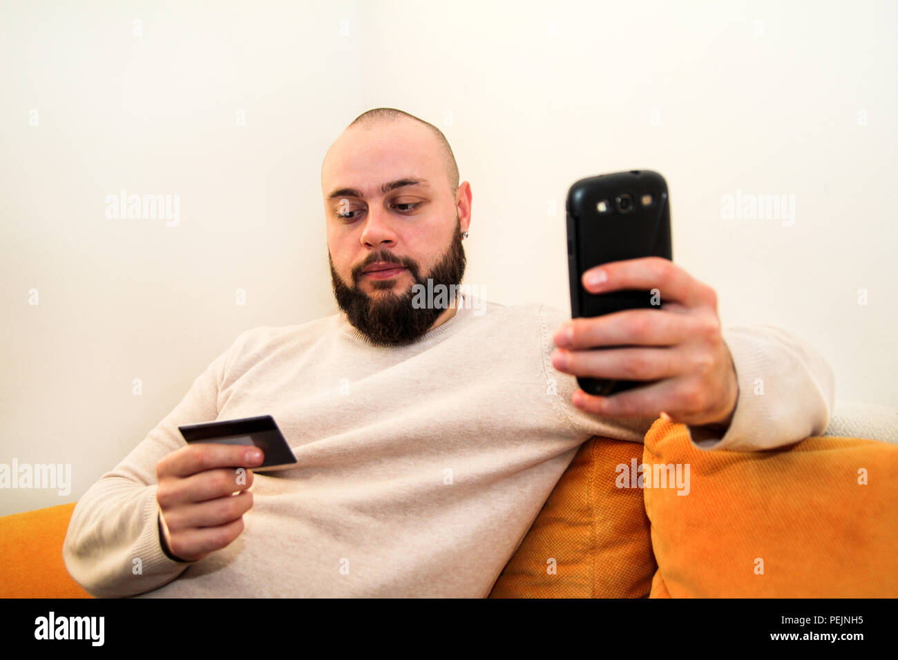 Uomo di pagare con carta di credito su smart phone presso l'ufficio domestico. Foto Stock