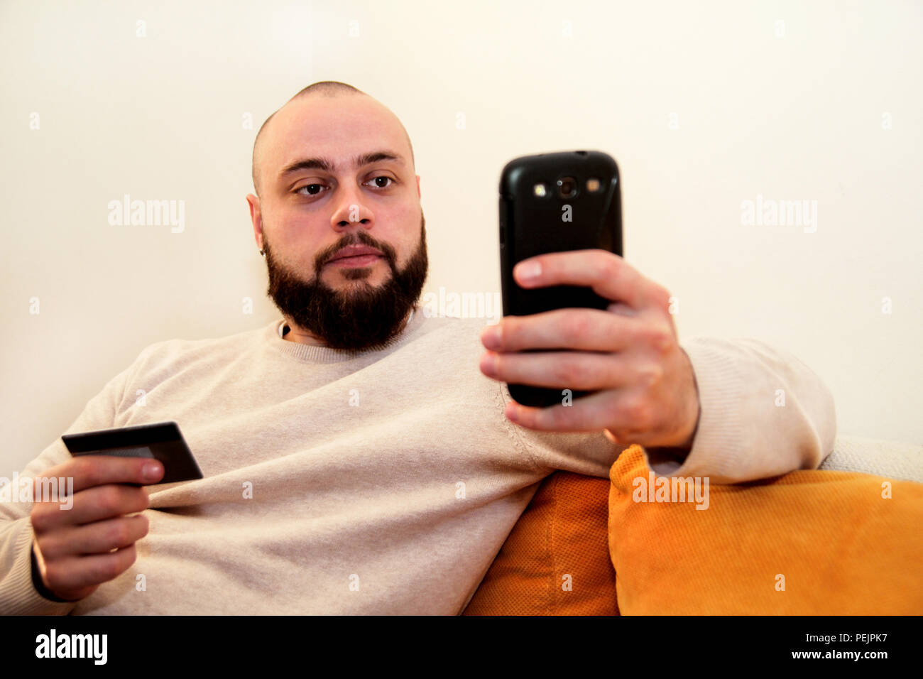 Uomo di pagare con carta di credito su smart phone presso l'ufficio domestico. Foto Stock