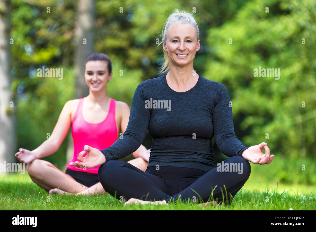 Montare maturo medio sani di età femmina insegnante di yoga yogi insegnamento giovane donna alla pratica dello yoga al di fuori di una naturale tranquillo ambiente verde Foto Stock