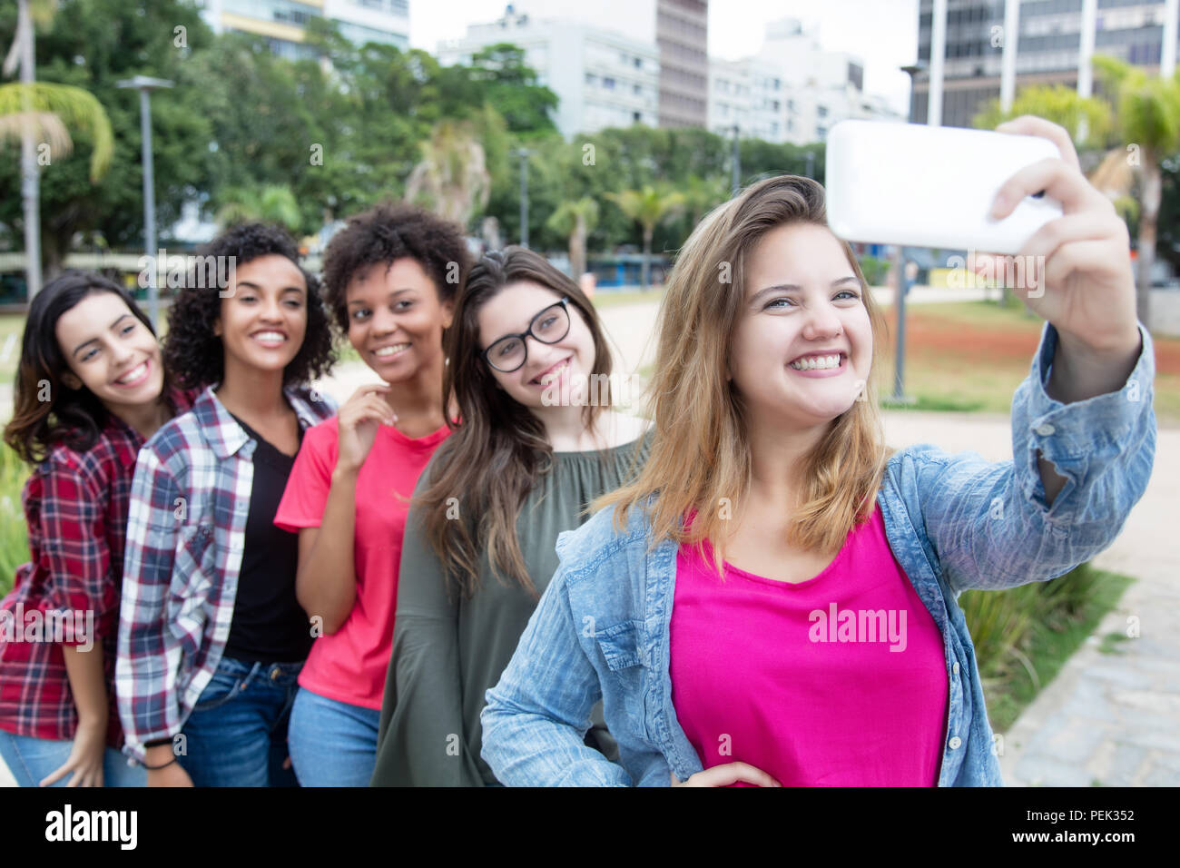 Bionda donna caucasica tenendo selfie con gruppo di amiche internazionale all'aperto in estate in città Foto Stock