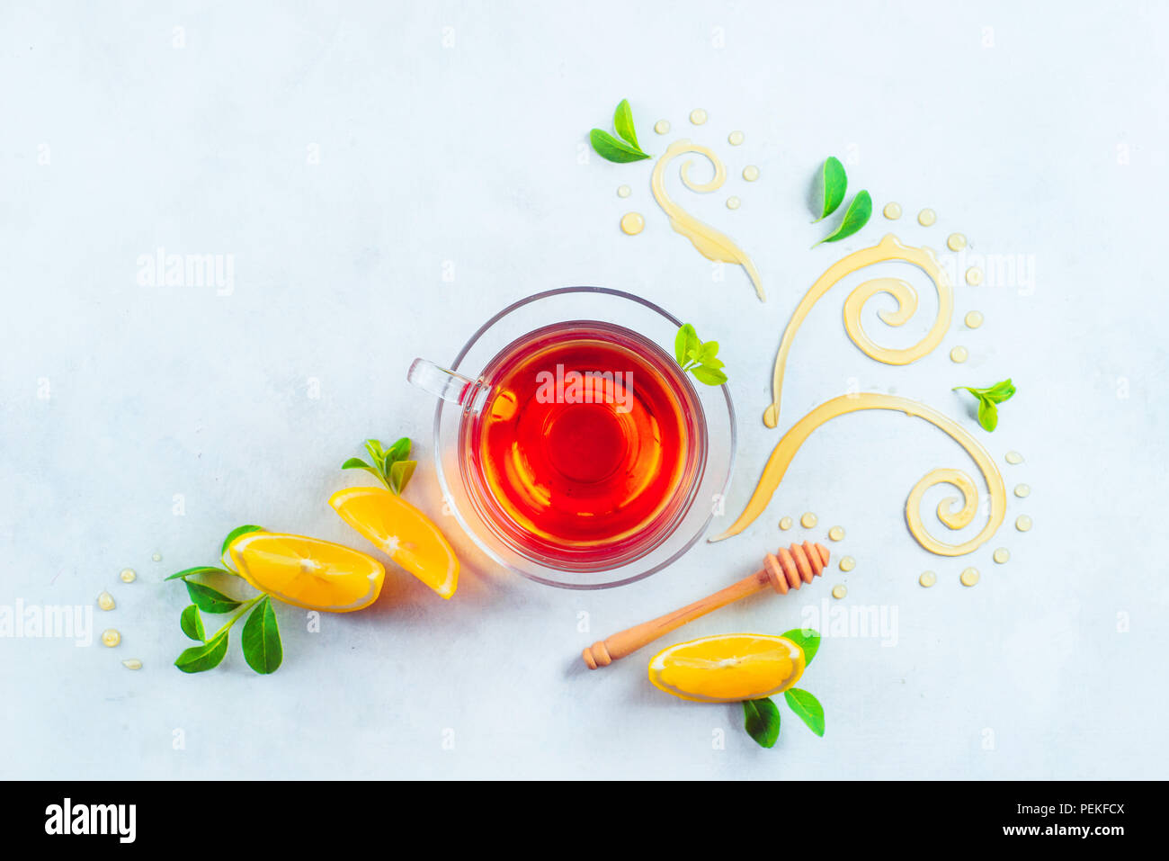Bicchiere di vetro di tè con miele decorativo volute, le fette di limone e foglie verdi. Casa rimedi flat giaceva su un fondo bianco con spazio di copia Foto Stock