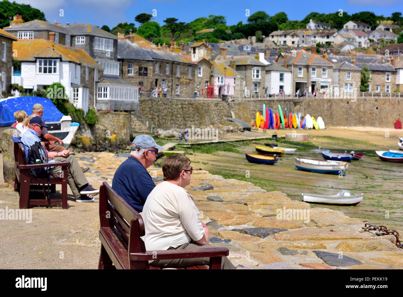 La gente seduta sulle panchine in estate sole nel villaggio di pescatori di Mousehole,Cornwall,l'Inghilterra,UK Foto Stock