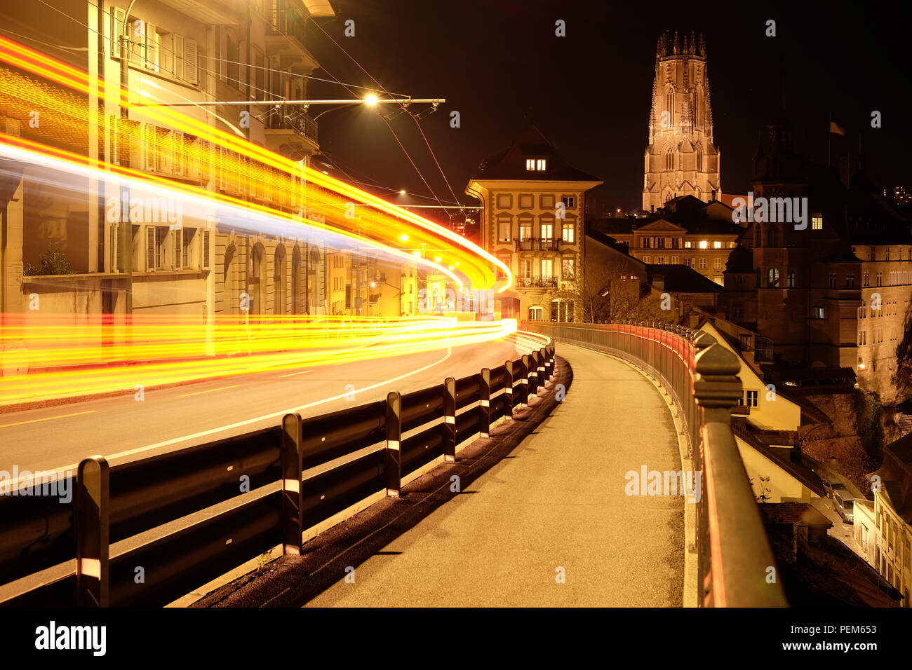 Una lunga esposizione night shot di Friburgo in Svizzera, con veicolo sentieri di luce sulla sinistra e la cattedrale di Saint-Nicolas in retro Foto Stock