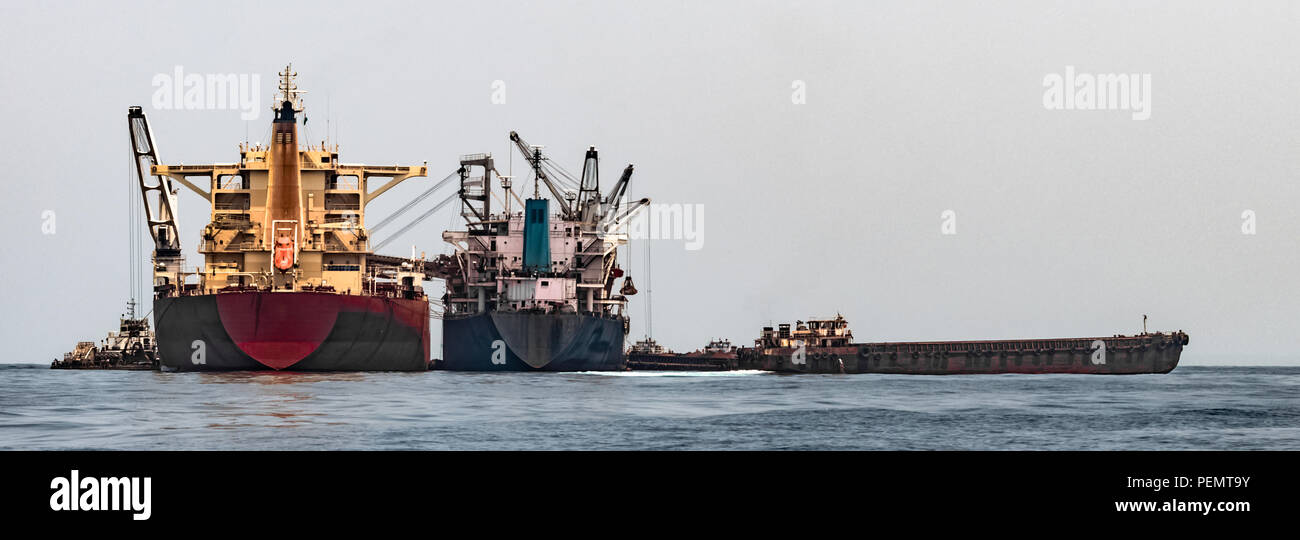 La visualizzazione completa delle gru galleggiante Transhipper nel processo di carico e scarico di una massa di minerale di ferro, cargo da e per l'alimentatore più piccolo peschereccio Foto Stock