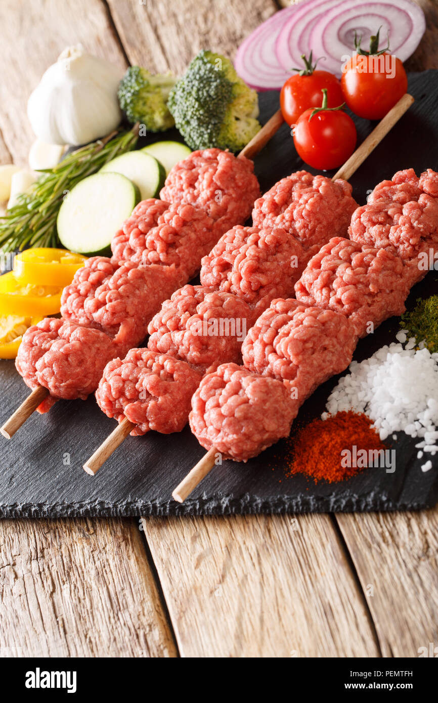 Turco kebab di greggio da carni macinate su spiedini con ingredienti e verdure vicino sul piano verticale. Foto Stock