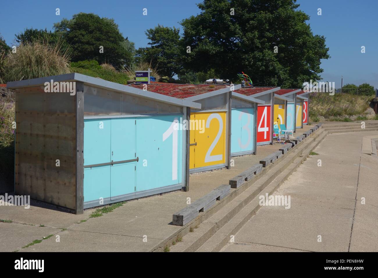 Nuova spiaggia capanne a Shoeburyness, sulla costa di Essex, con numeri in grassetto e colori primari tetti di Sedum di ciottoli e costruzione del pannello Foto Stock