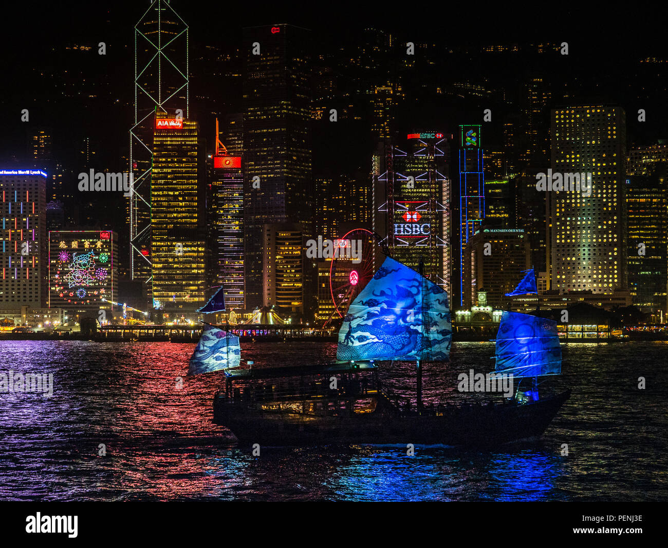 Hong Kong Waterfront di notte - il Aqua Luna II stile tradizionale Giunca Cinese passa davanti al porto edifici sul Porto Victoria Foto Stock