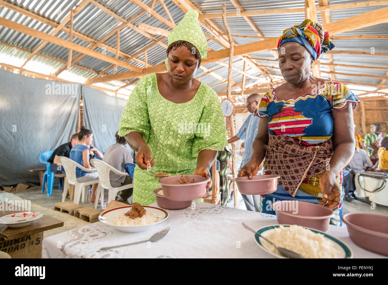 Due donne in abiti colorati servono cibo su piastre in Ganta, Liberia. Foto Stock