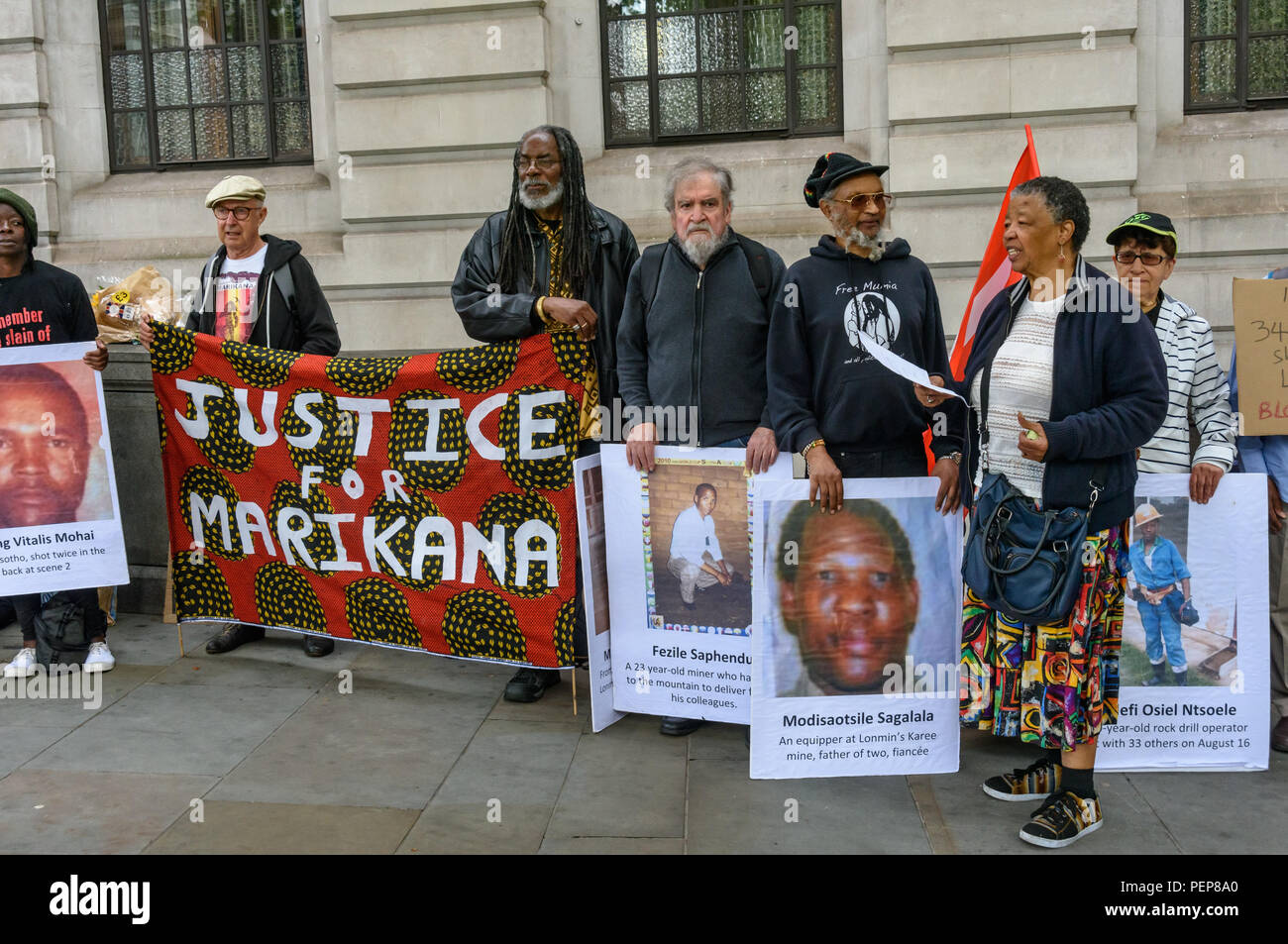 Londra, Regno Unito. Il 16 agosto 2018. Manifestanti tenere una veglia al di fuori del Sud Africana di Alta commissione in Trafalgar Square al sesto anniversario della strage quando 34 colpisce i minatori sono stati uccisi dalla polizia sudafricana a Lonmin Marikana della miniera di platino. Dopo i discorsi circa l'evento, i nomi dei 34 vittime sono state lette e grandi fotografie di essi mettere sulla parte anteriore dell'Ambasciata lungo con flowere. Anche se le prove contro la polizia era chiaro, 19 scioperanti sono stati cambiati con l' omicidio e gli altri detenuti per altri reati. Credito: Peter Marshall / Alamy Live News Foto Stock