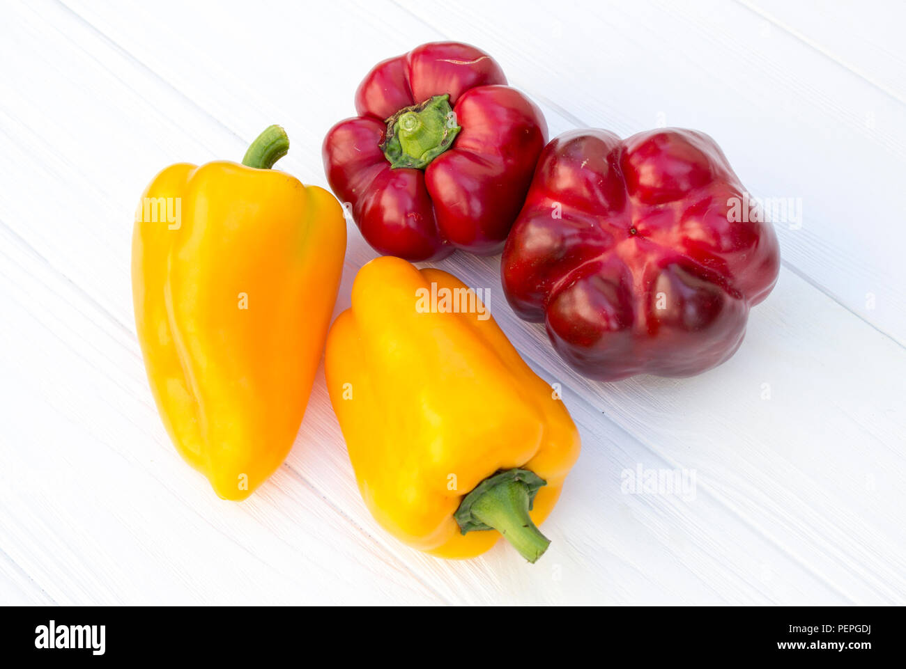 Rosso e giallo pepe su un bianco sullo sfondo di legno Foto Stock
