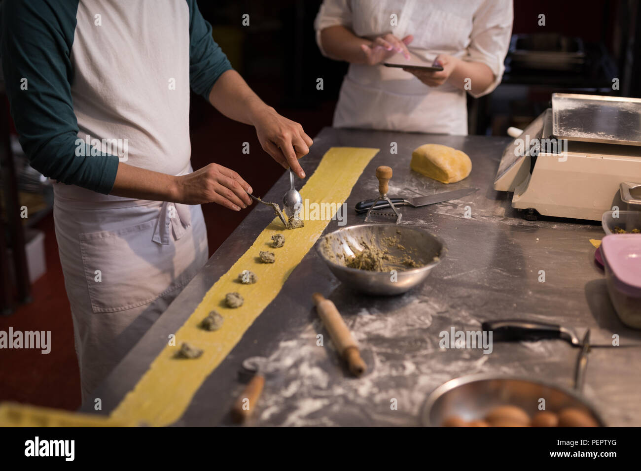 Baker preparare la pasta mentre co-lavoratore utilizzando tavoletta digitale il suo accanto a Foto Stock