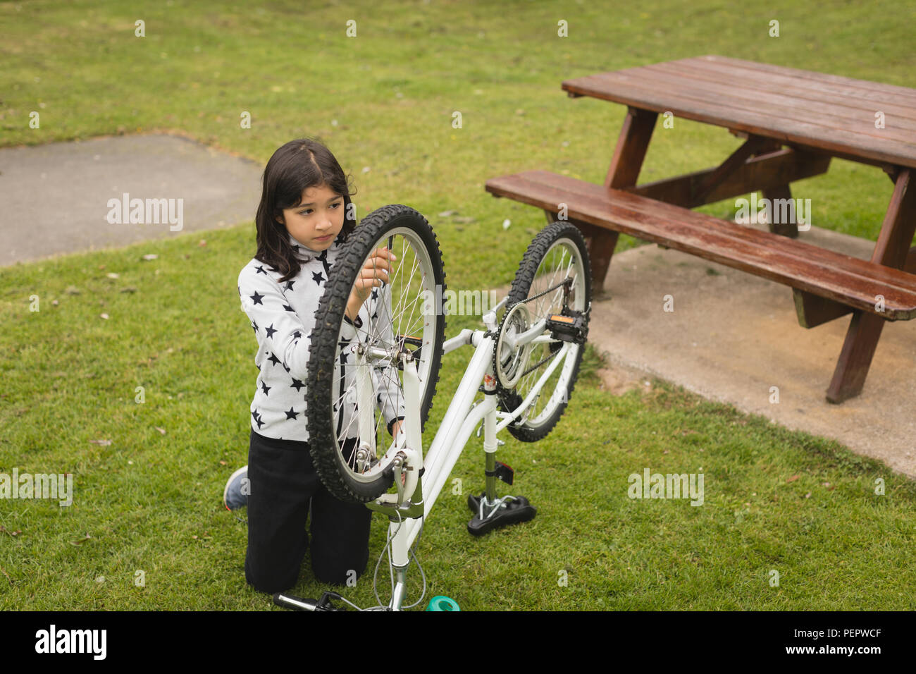 Ragazza riparazione bicicletta al giardino Foto Stock
