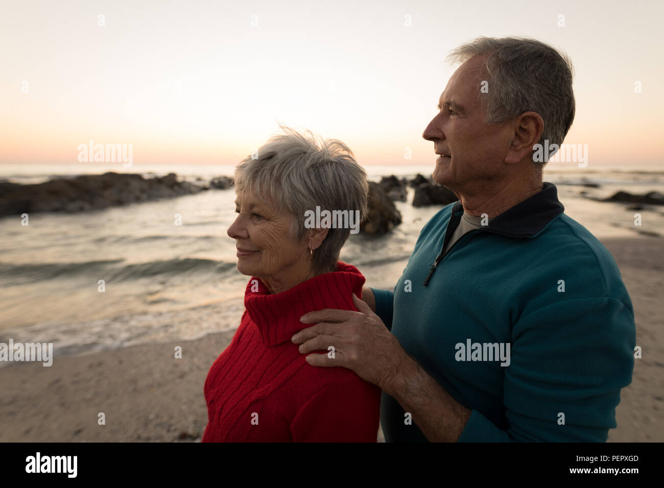 Coppia senior permanente sulla spiaggia durante il tramonto Foto Stock