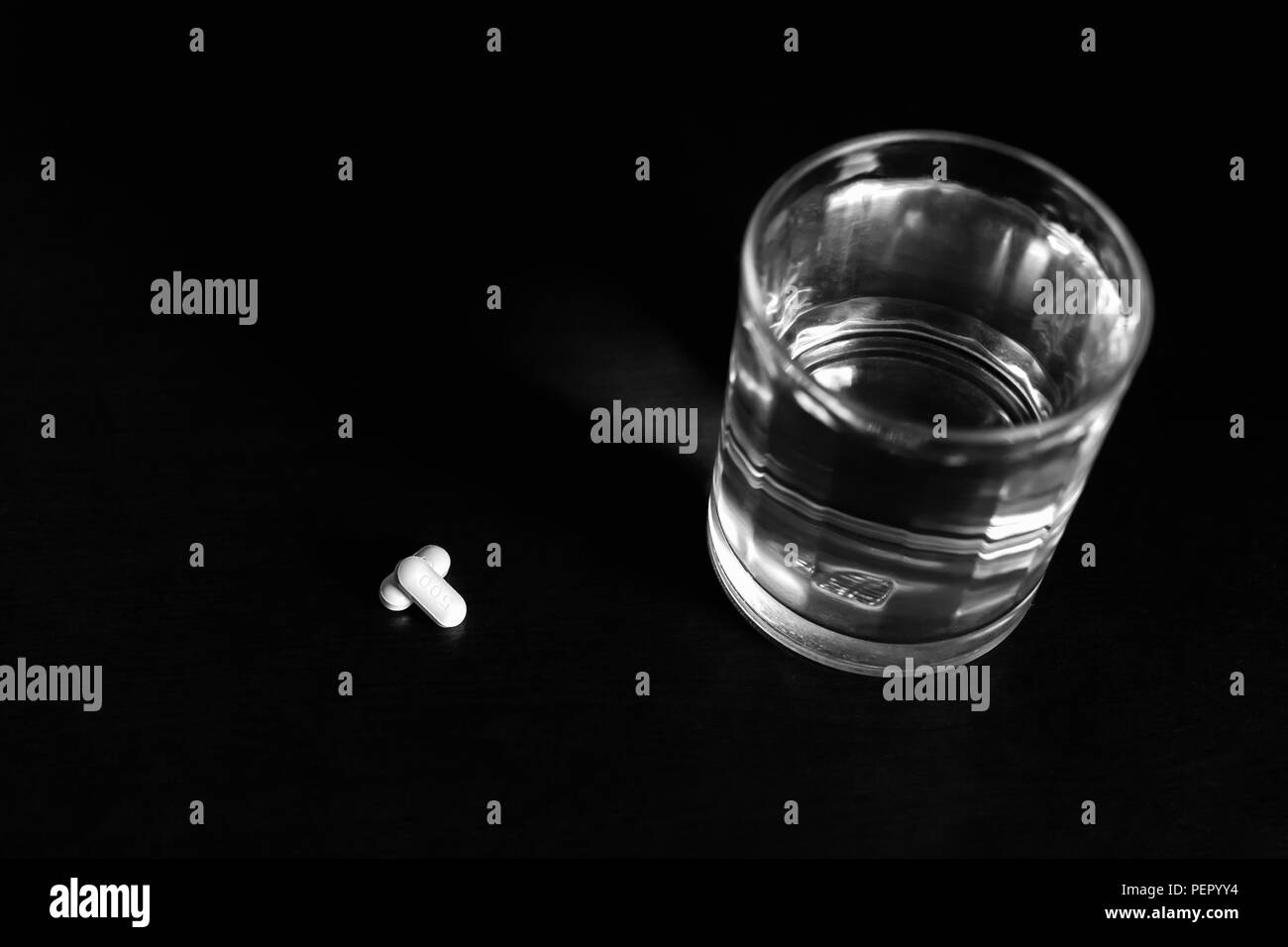Vetro concettuale di acqua e pillole sul tavolo di legno in bianco e nero nel filtro di colore blu. Foto Stock