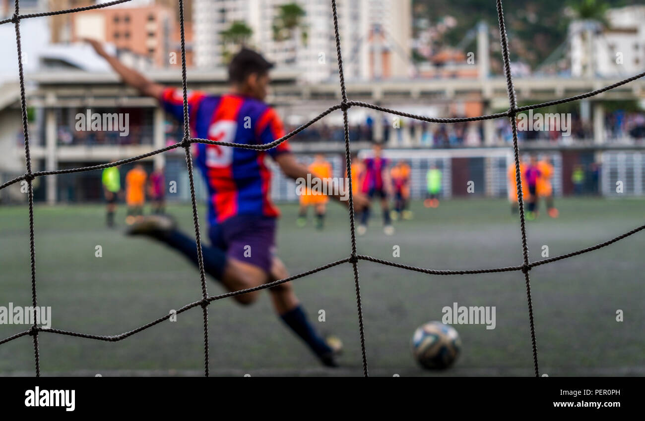 Un ragazzo calci ad un pallone da calcio, concentrarsi solo sulla rete di prua, ma il ragazzo può essere chiaramente visto calciare la palla Foto Stock