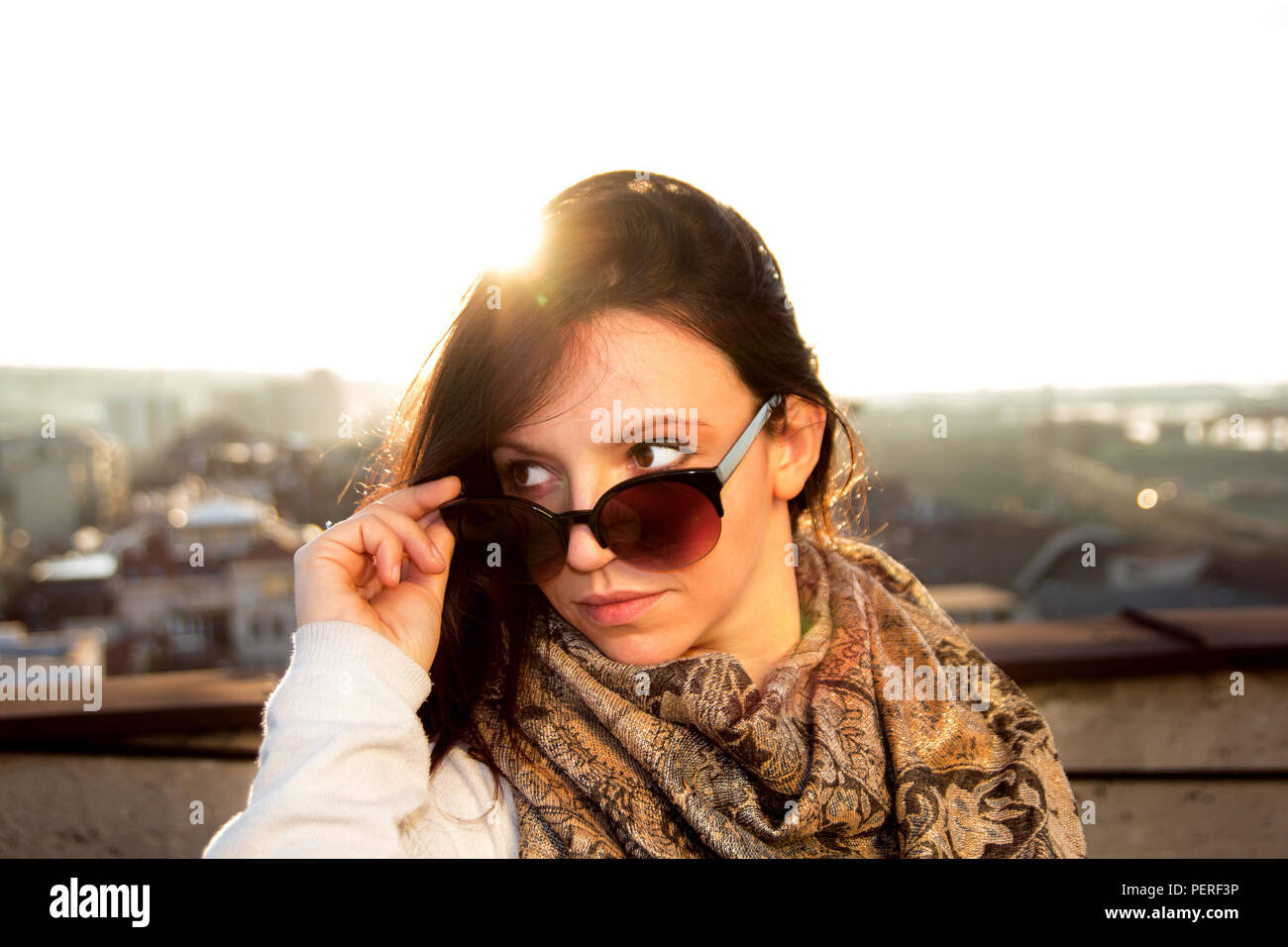 Bella ragazza giovane con occhiali da sole in amore per godersi il sole e  in posa sul tetto. Nello sfondo il panorama della città Foto stock - Alamy