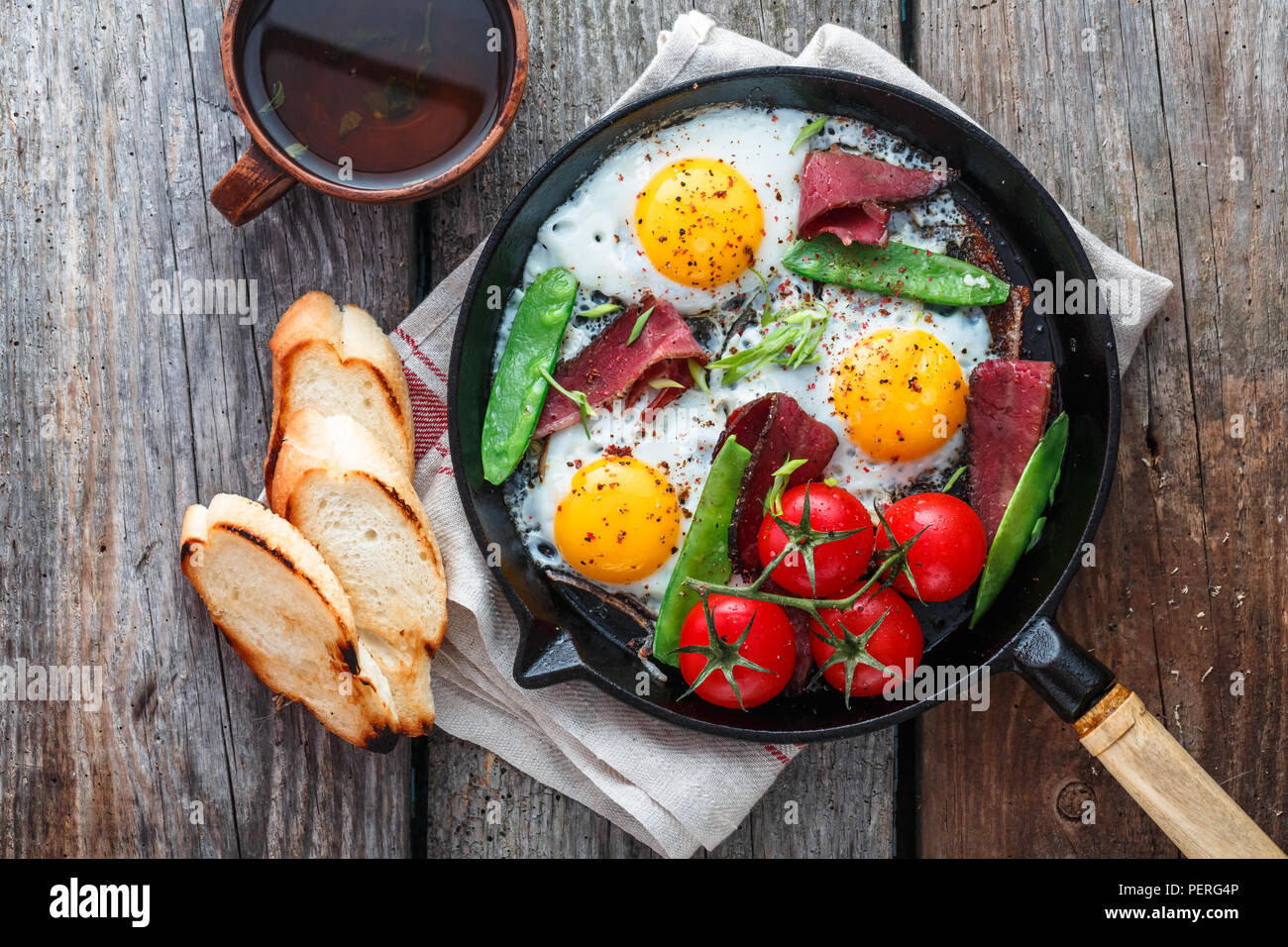 Uova fritte in padella con pomodorini, piselli verdi e pastrami. Copyspace Foto Stock