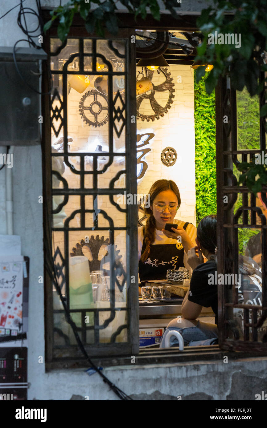 Suzhou, Jiangsu, Cina. Cameriera con un telefono cellulare all'interno di una caffetteria sulla strada Shantang. Foto Stock