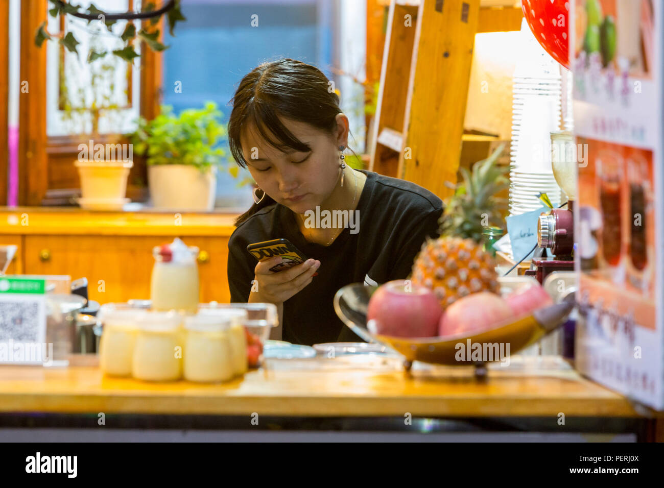 Suzhou, Jiangsu, Cina. Cameriera con un telefono cellulare all'interno di una caffetteria sulla strada Shantang. Foto Stock