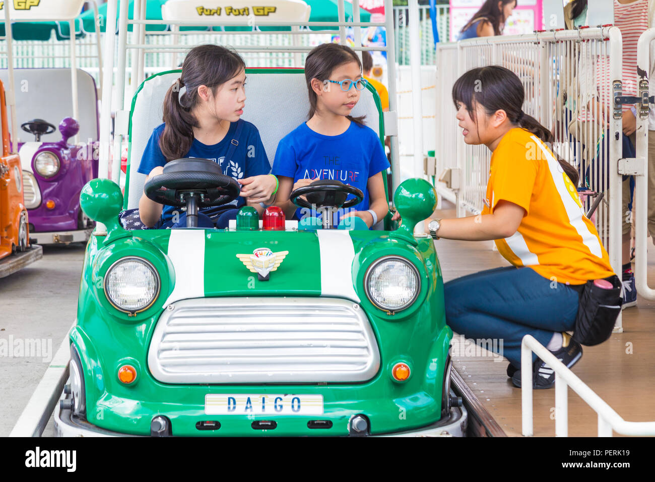 TOKYO, Giappone - 19 Luglio 2016 - femmina giapponese Tokyo Dome Parco Divertimenti personale spiega a due ragazze asiatiche come cavalcare su un Furi Furi GP auto a Tokyo D Foto Stock
