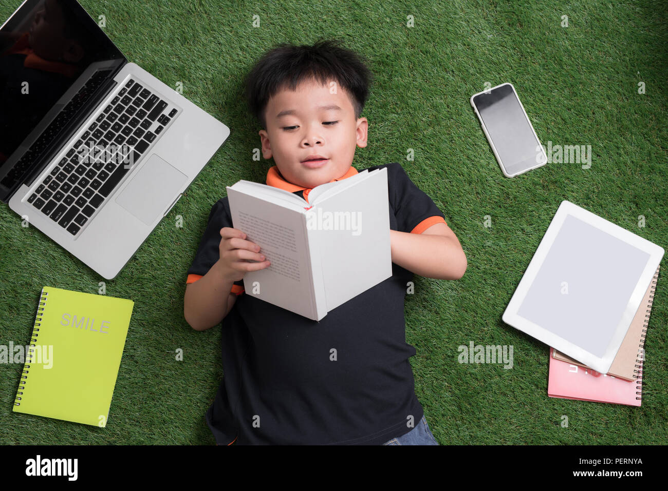 A sette anni di età bambino leggendo un libro sdraiati sull'erba Foto Stock