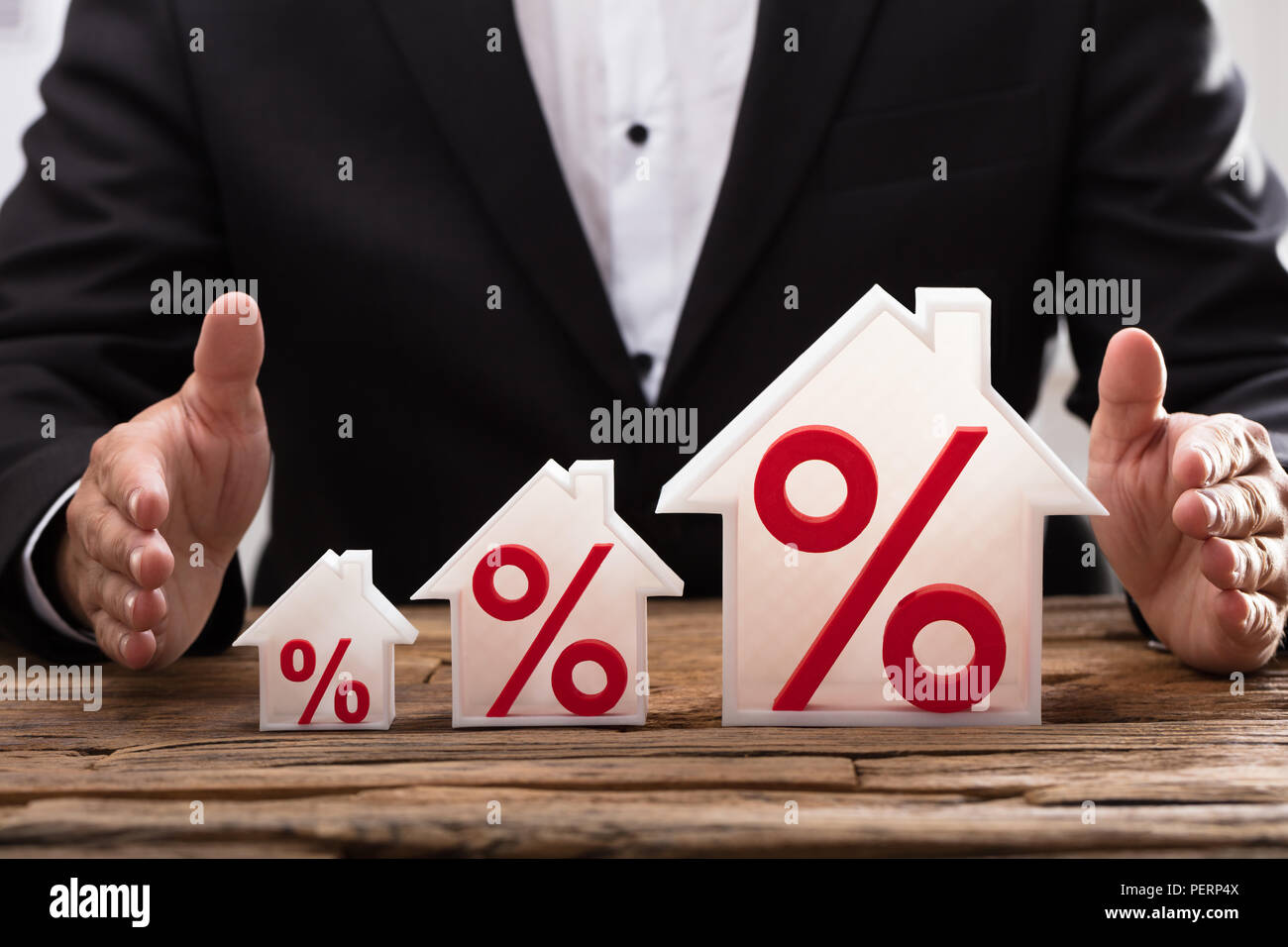 Close-up di un imprenditore della mano aumentando la protezione di modelli della casa rosso con simboli di percentuale Foto Stock