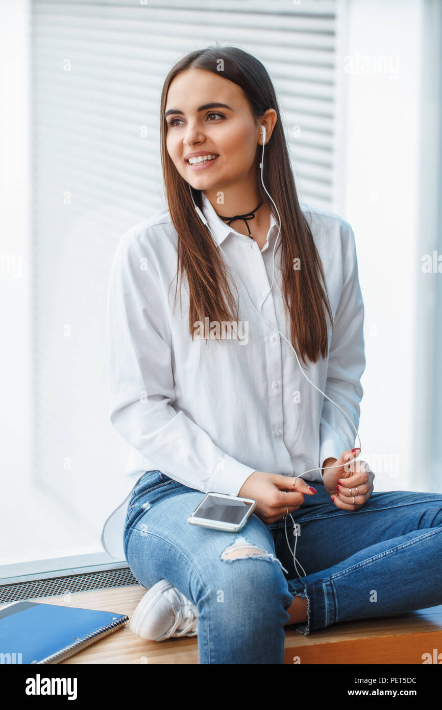 Ritratto di giovane bella ed elegante ragazza caucasica donna in maglia  bianca e jeans blu seduta sul davanzale in college university ascolto di  musi Foto stock - Alamy