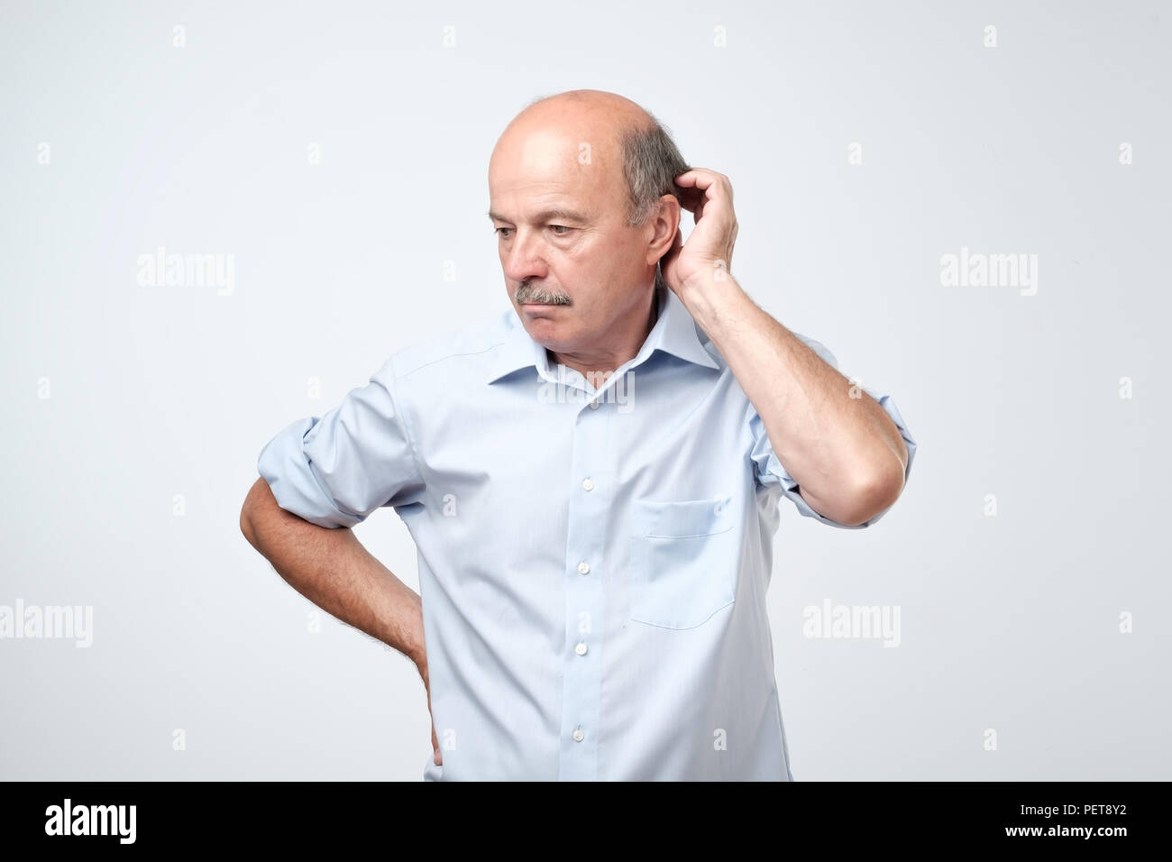 Bald uomo maturo con baffi in maglietta blu soffre di indecisione tenendo le mani vicino alle guance. Egli non sa come prendere la giusta decisione Foto Stock Bald uomo maturo con baffi in maglietta blu soffre di indecisione tenendo le mani vicino alle guance. Egli non sa come prendere la giusta decisione Foto Stock