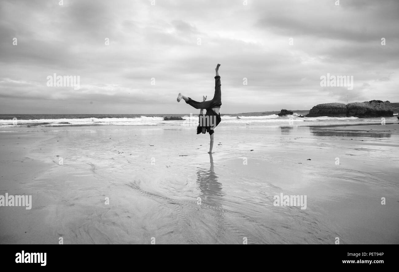 Giovane uomo su un wet spiaggia sabbiosa facendo acrobazie, immagine monocromatica Foto Stock