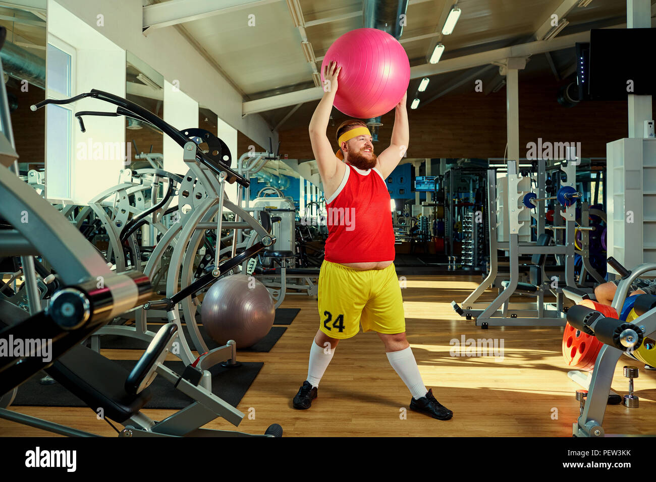 Un divertente uomo grasso facendo esercizi in palestra. Foto Stock