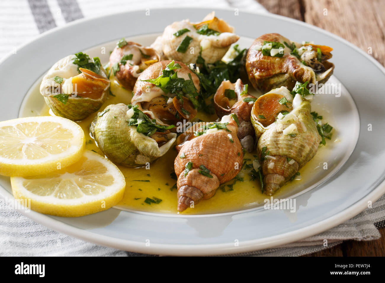 Porzione di lumache di mare con salsa di burro, aglio e prezzemolo, limone vicino sul tavolo orizzontale. Foto Stock