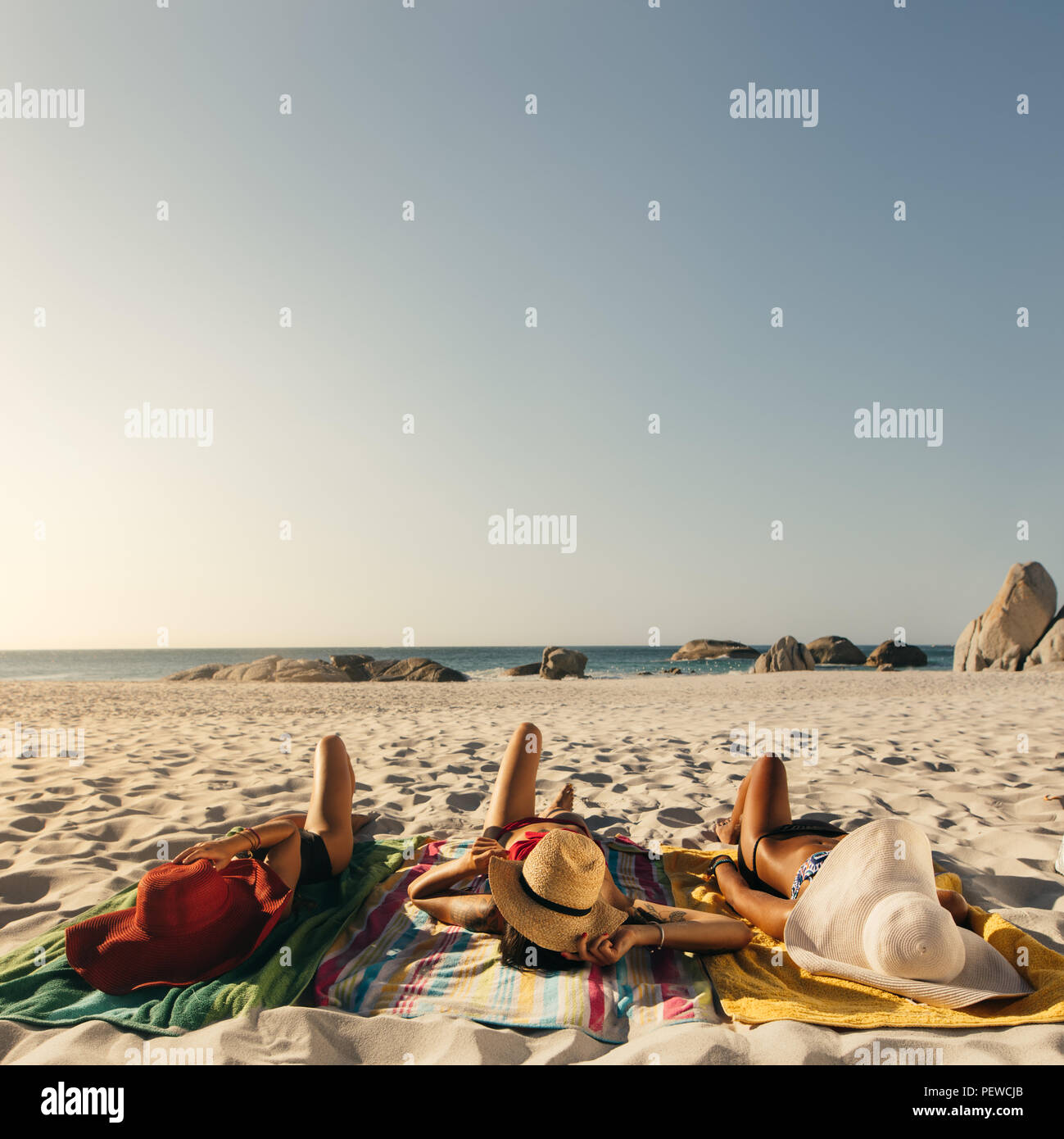 Vista posteriore delle donne in bikini a prendere il sole sdraiati sulla  spiaggia indossando cappelli di sun. Tre amiche in vacanza di relax presso  una spiaggia di indossare cappelli Foto stock -