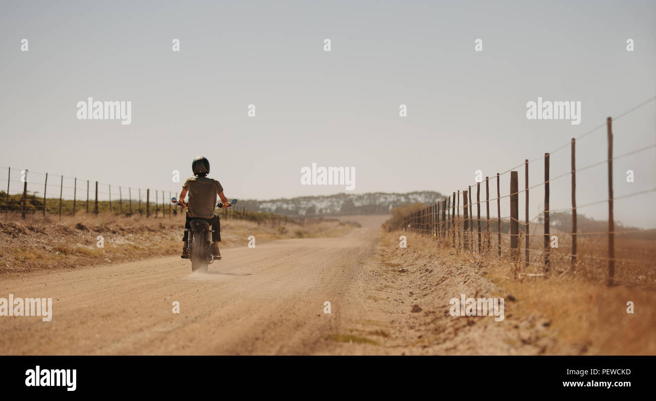 Vista posteriore dell'uomo a cavallo del ciclo del motore su una strada di campagna. Motociclista sposta lungo una strada di campagna. Foto Stock
