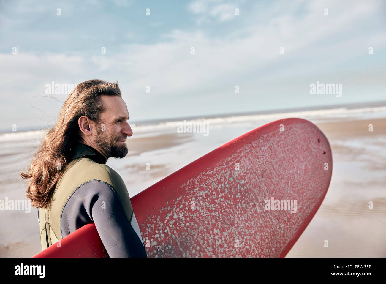 Uomo con una dimensione completa della tavola da surf permanente sulla spiaggia affacciata sul mare Foto Stock
