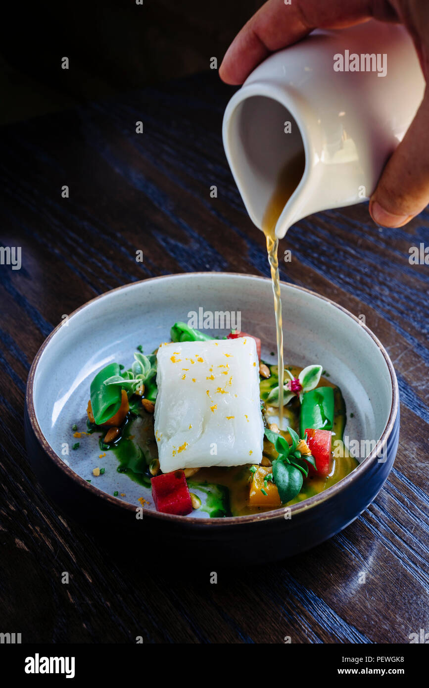 Versare il brodo di halibut al limone, piselli, melone, barbabietole e le erbe aromatiche Foto Stock