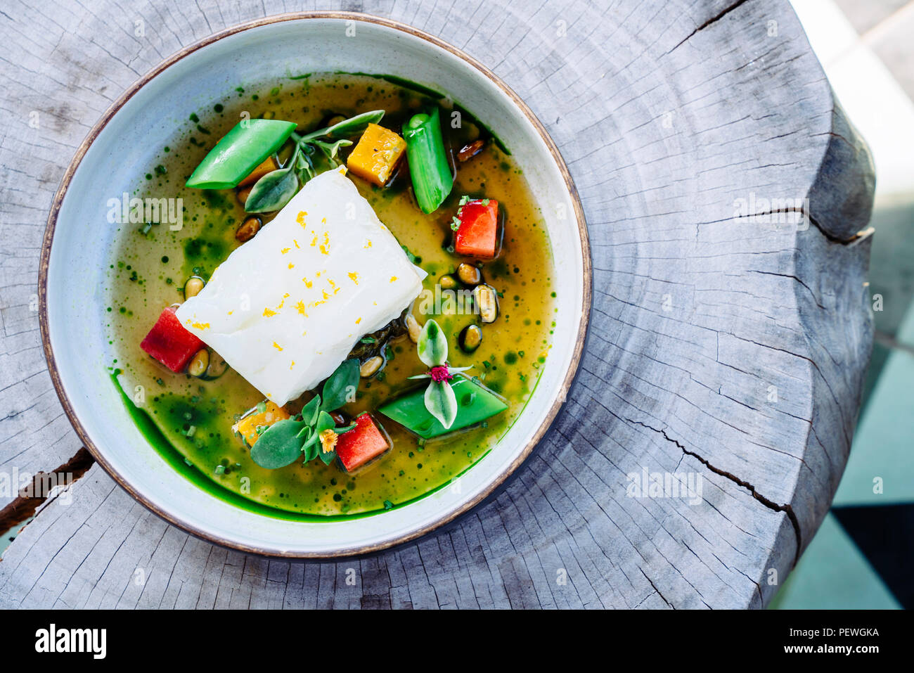 Versare il brodo di halibut al limone, piselli, melone, barbabietole e le erbe aromatiche Foto Stock