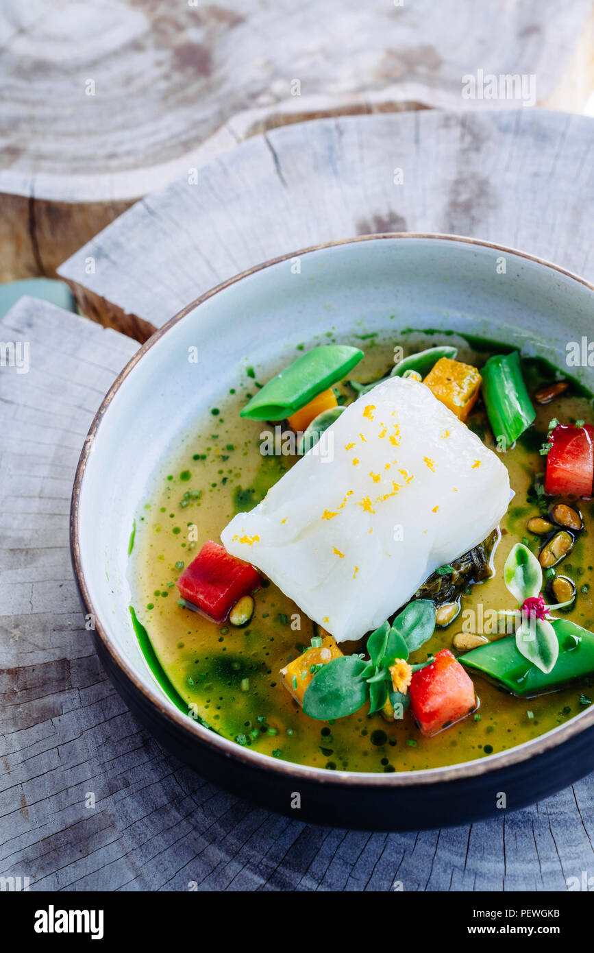 Versare il brodo di halibut al limone, piselli, melone, barbabietole e le erbe aromatiche Foto Stock