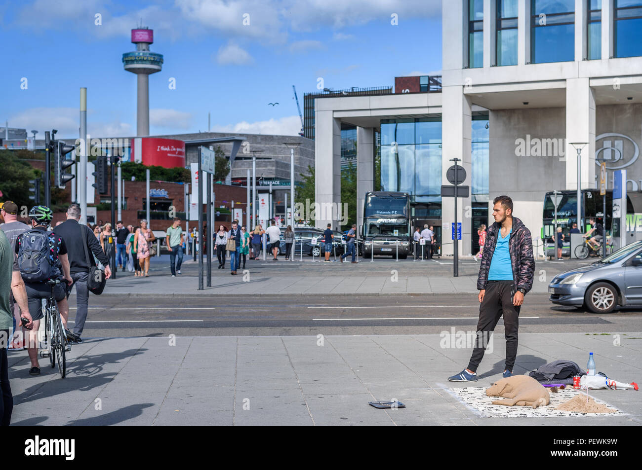 Un artista di strada con la scultura di sabbia di un cane nel centro di Liverpool come i pedoni attraversano la strada. Foto Stock