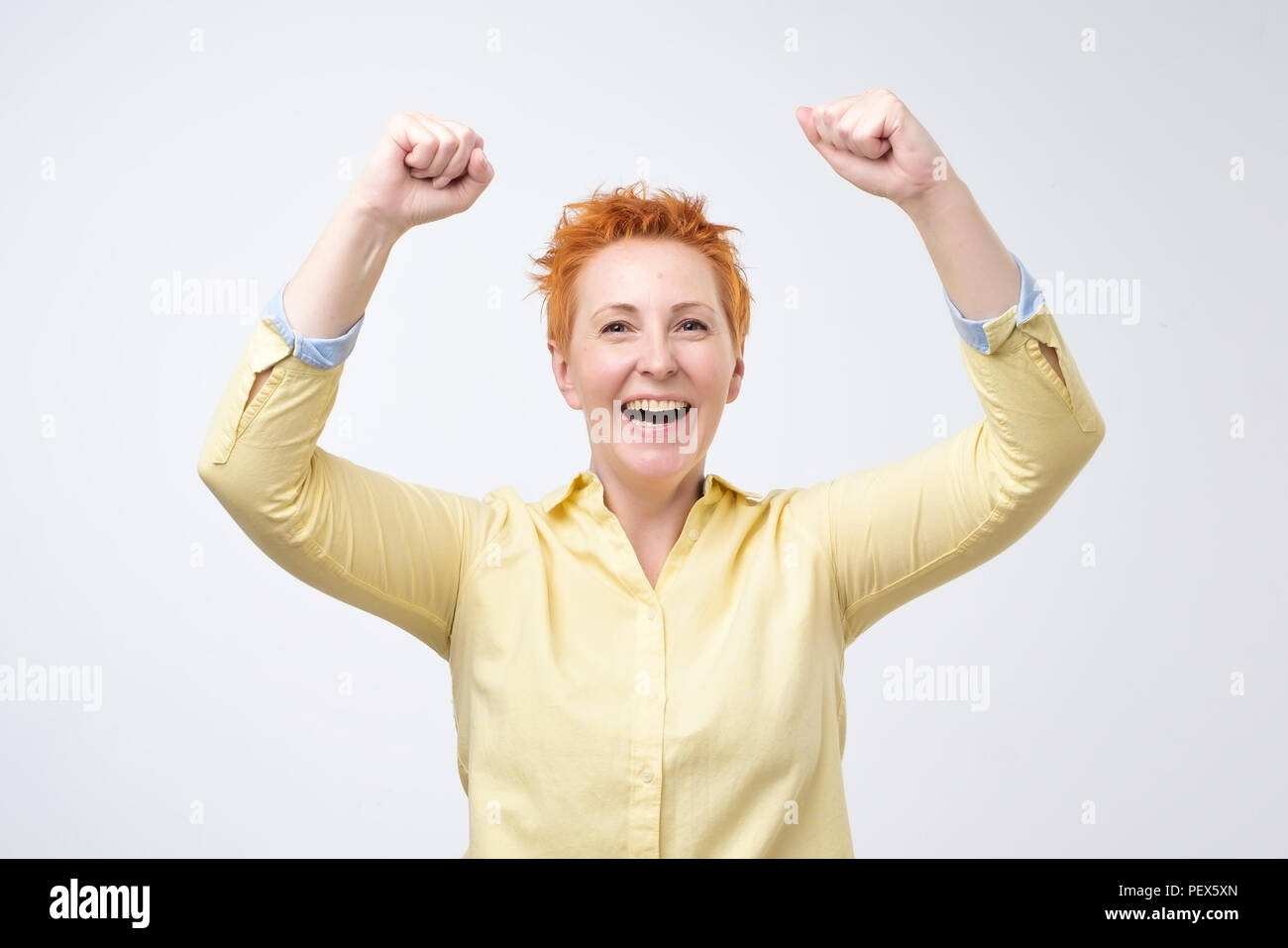 Felice caucasian donna con capelli rossi esulta pugni di pompaggio entusiasta celebra il successo. Ho fatto questo concetto di WOW Foto Stock