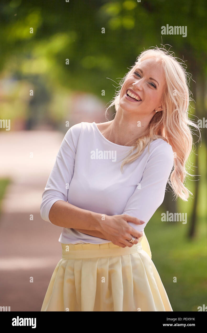 Una giovane donna ritratto, 25 anni, abito giallo, top bianco, parco, sorridendo felice. Foto Stock