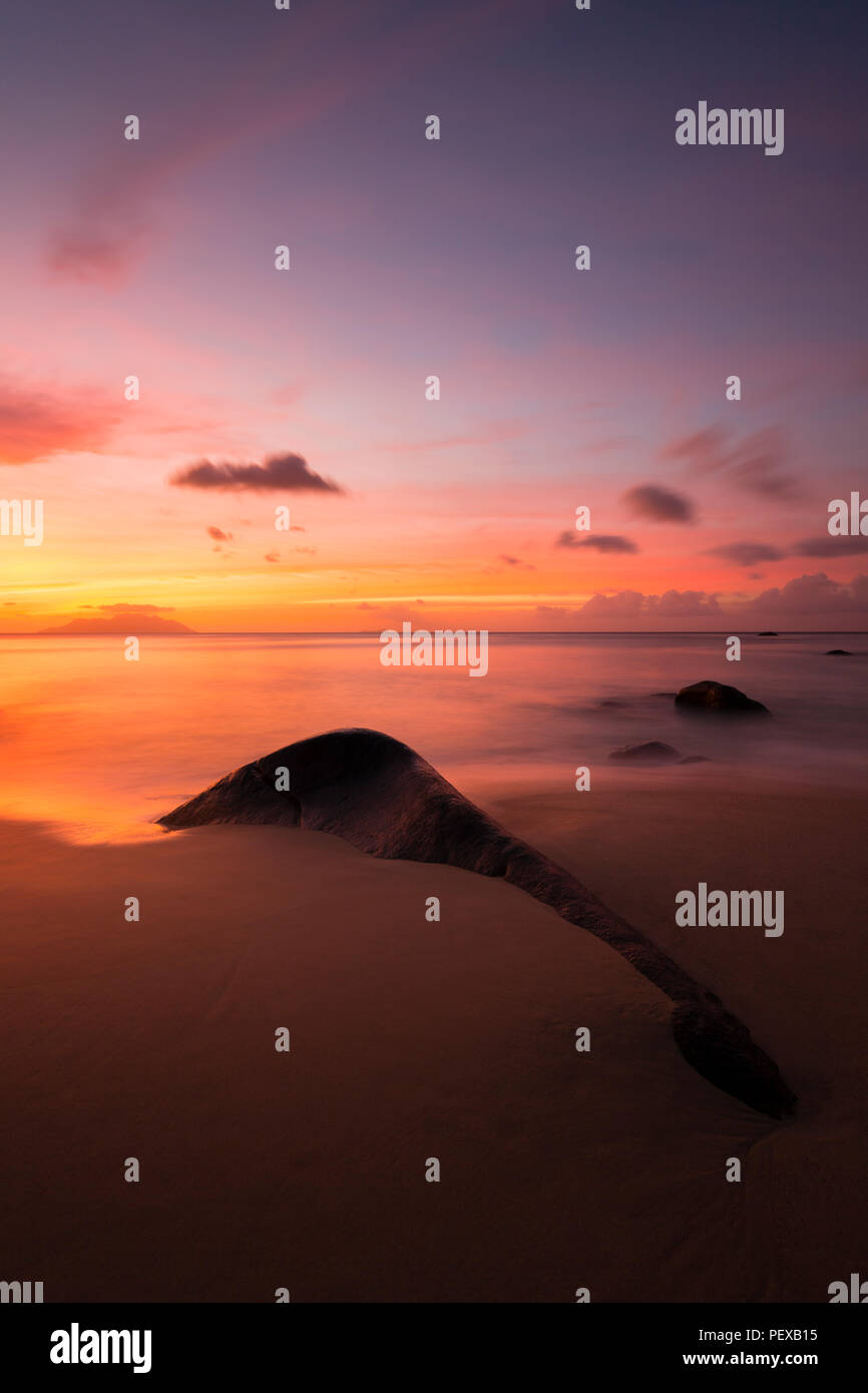 Tramonto colorato lunga esposizione colpo al Sunset Beach in Mahe in Seychelles con una roccia di granito in primo piano. Foto Stock