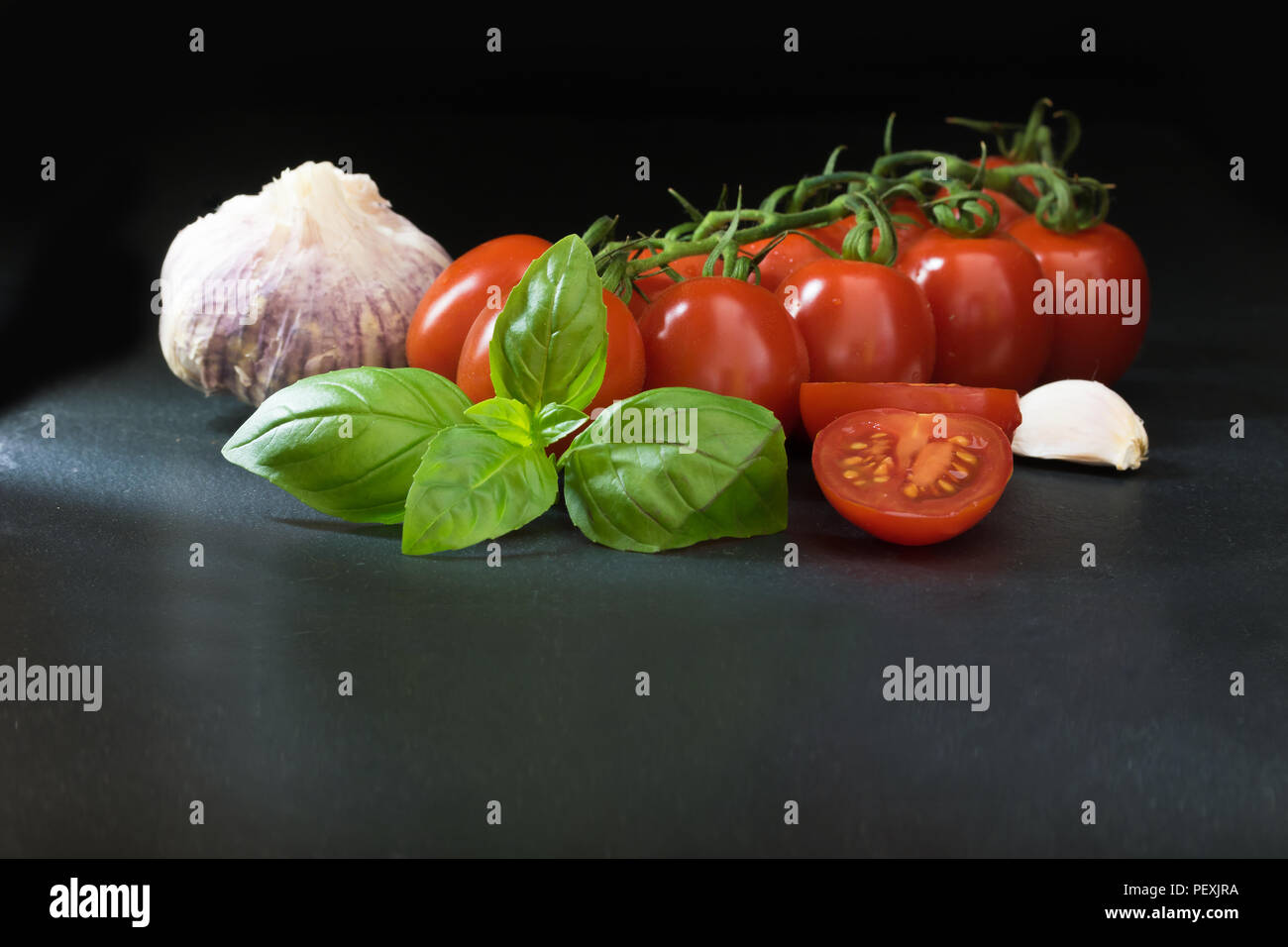 Tasto basso colpo di arbusti di pomodoro, basilico e aglio giacente sulla pietra nera table.Tutto su sfondo scuro. Foto Stock