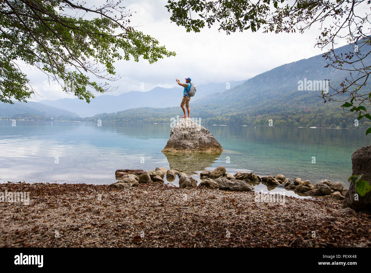 Uomo di scattare una foto mentre si sta in piedi sul rock in riva al lago di Bohinj, il Parco Nazionale del Triglav, Slovenia Foto Stock