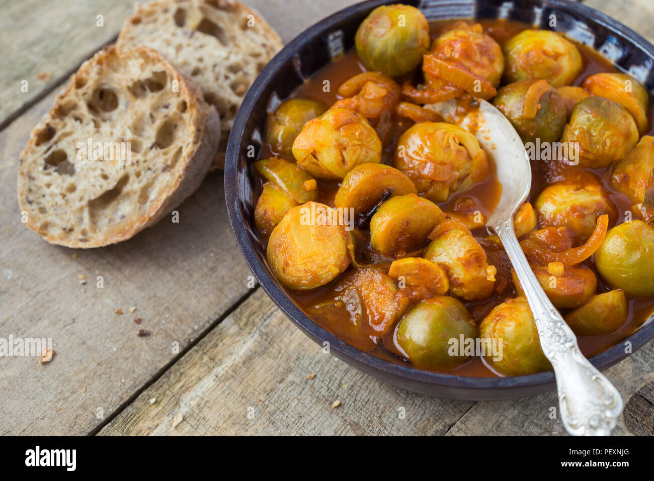 Arrosto di freschi Cavoli di Bruxelles in ceramica artigianale ciotola di legno naturale dello sfondo. Foto Stock