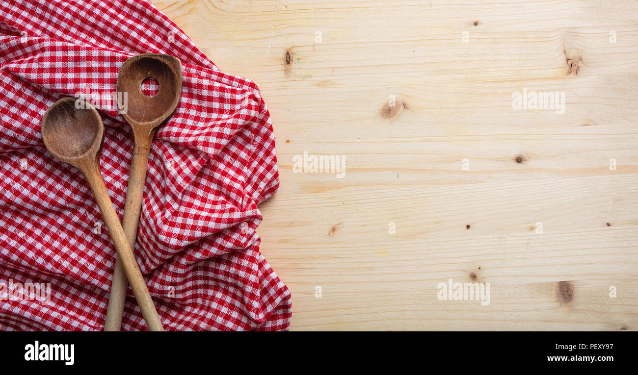 Cucina in legno utensili e di colore rosso e bianco a scacchi tovaglia da picnic sul tavolo di legno, vista dall'alto, spazio di copia Foto Stock