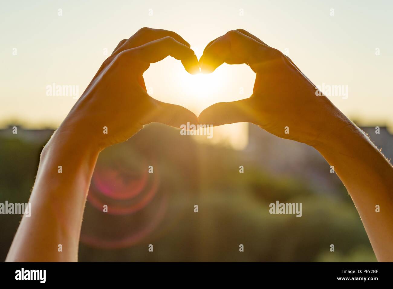 Mani mostrano il gesto di cuore, sfondo tramonto di sera, la silhouette della città Foto Stock
