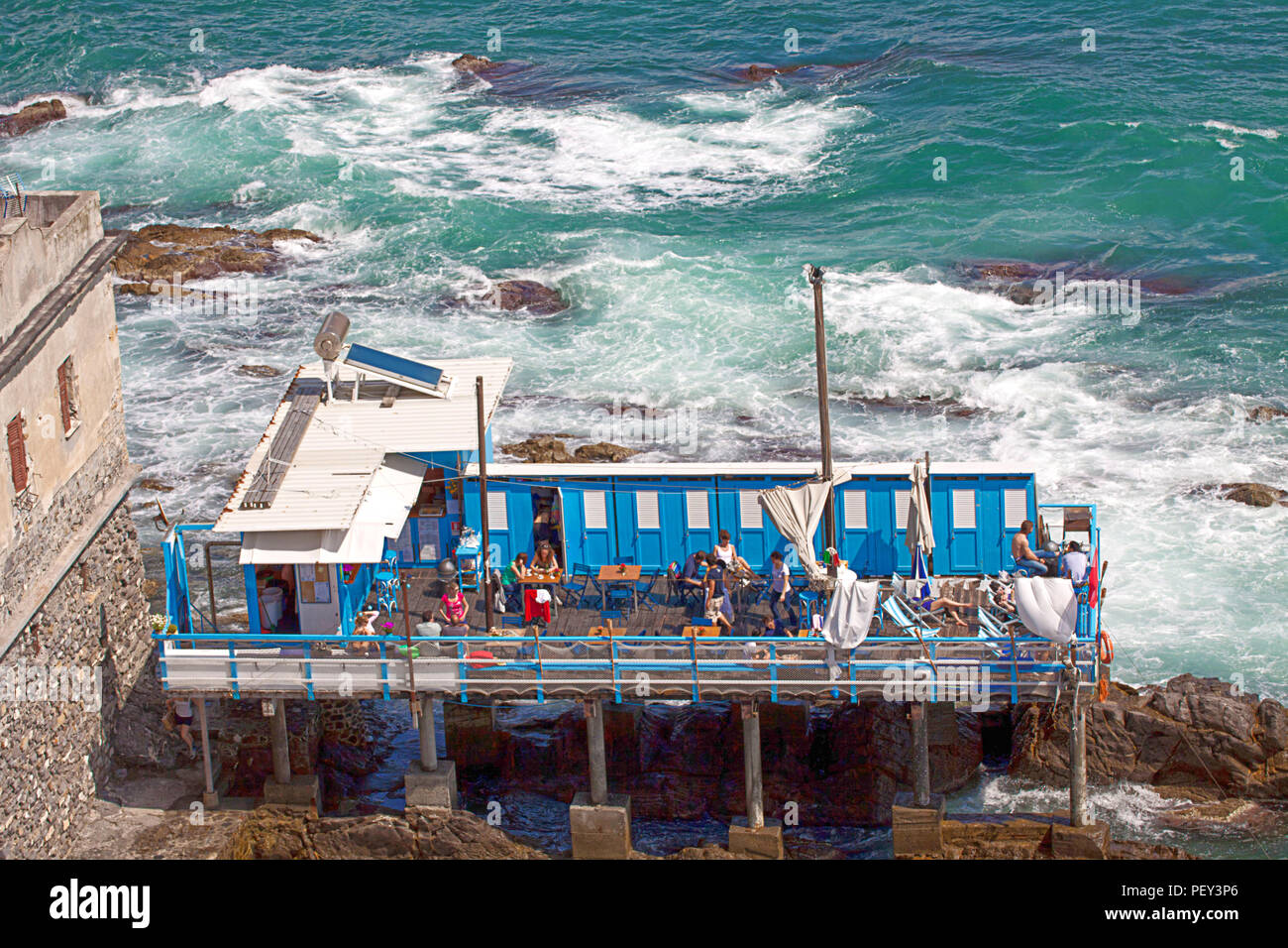 GENOVA, Italia - Le persone godono di rilassarsi e prendere il sole in un piccolo stabilimento bagno con cabine hanging off la scogliera di fronte al mare Foto Stock