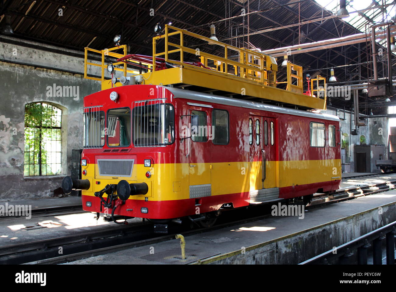 Restaurato antico retrò dalla vecchia linea ferroviaria i fili elettrici di rosso e di giallo riparare locomotore parcheggiato nel vecchio fatiscente stazione ferroviaria edificio utilizzato come mechan Foto Stock