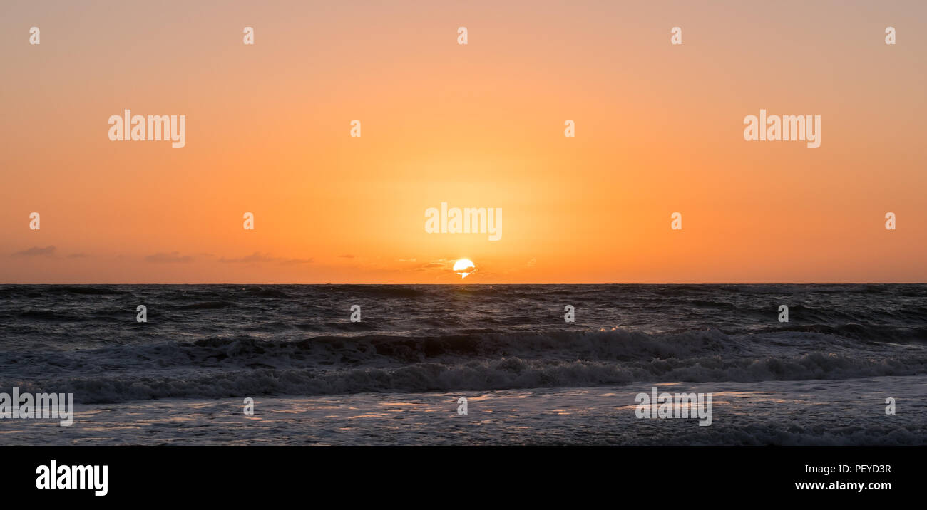 Foto della posizione centrata sunrise in una spiaggia con un arancione e rosa del cielo. Foto Stock