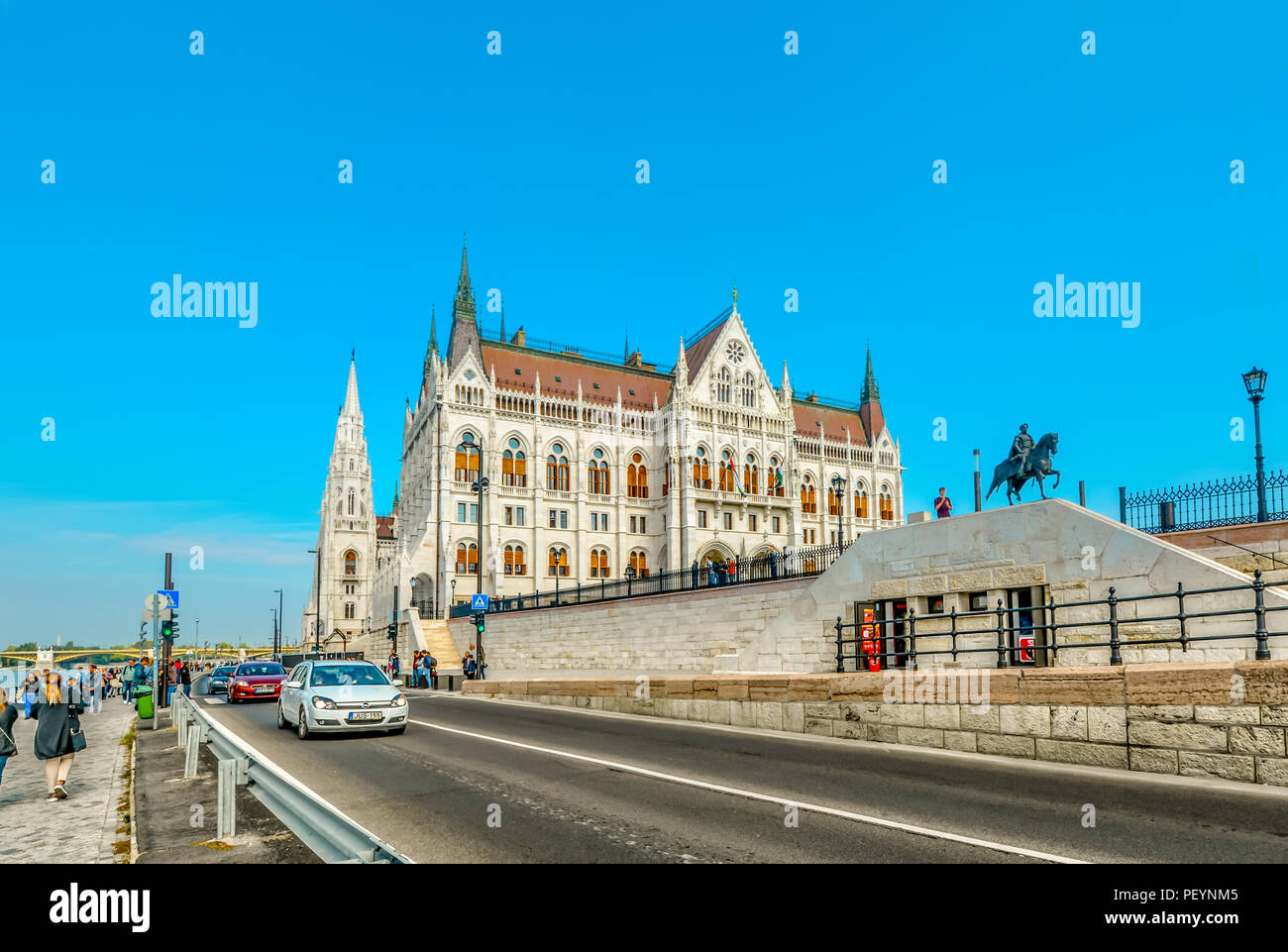Turisti e le automobili viaggiano waterfront avenue lungo il fiume Danubio con il Parlamento ungherese edificio in vista a Budapest, Ungheria Foto Stock